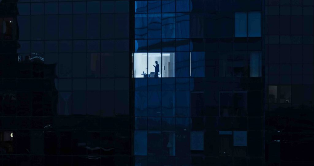 Aerial Shot: From Outside into Office Building with Businessman Using Mobile Phone and Standing by the Office Window. Beautiful Shot of The Financial Business District Skyscrapers.